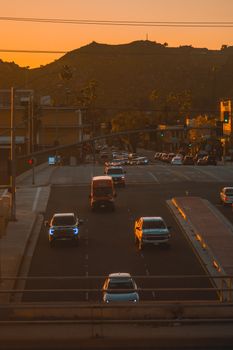 A lively city street at sunset with cars driving and warm orange hues filling the scene.