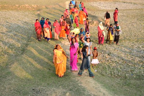 Free Indian women in colorful sarees walk through a field carrying pots, showcasing cultural traditions. Stock Photo