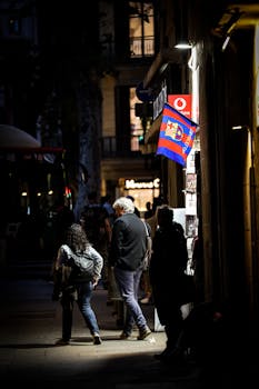 A street scene in Barcelona at night with people walking under a flag.
