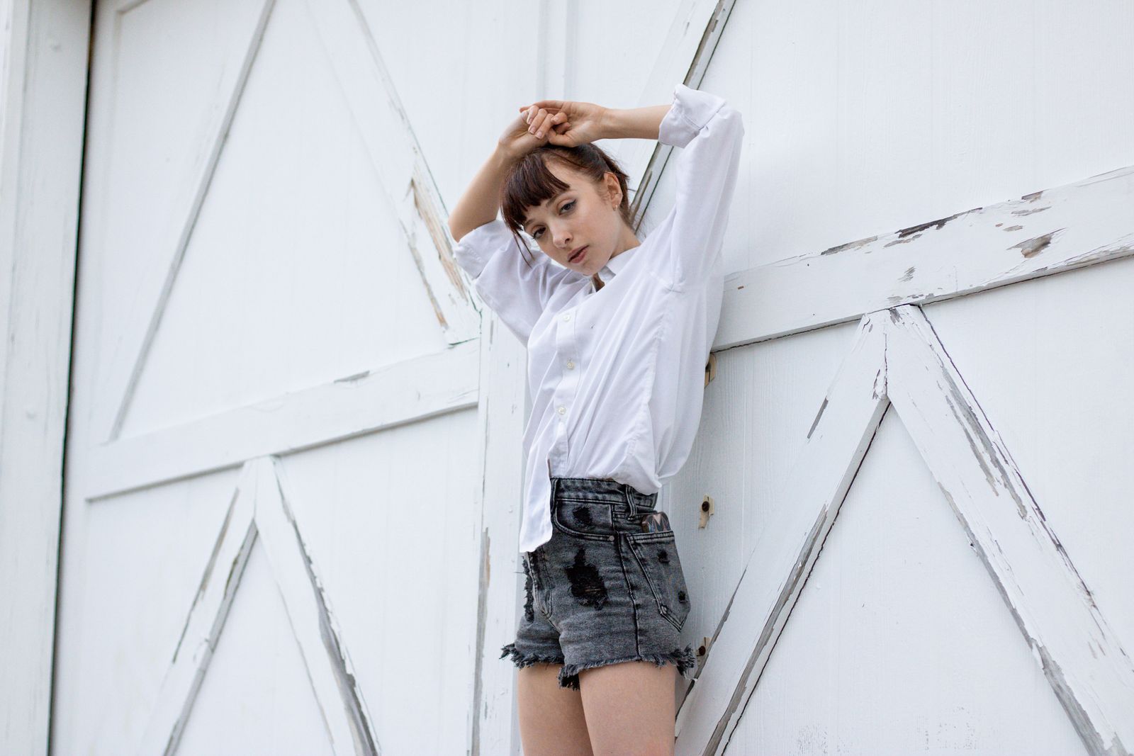 Denim shorts outfits 2026 — a woman in chic denim shorts posing against a white wooden door, the elegant way to wear denim shorts