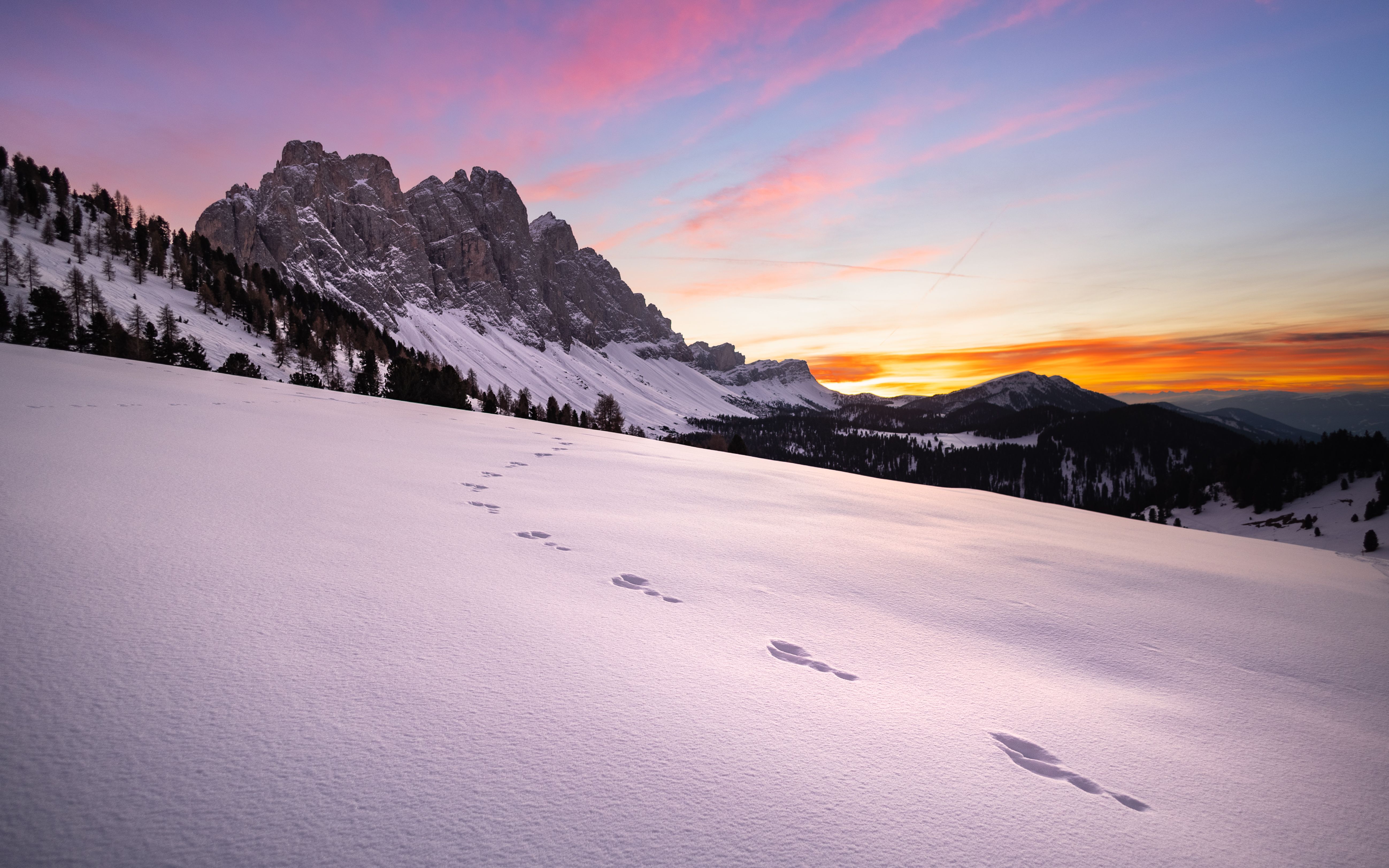Animal tracks across an open snowfield below rock towers at sunset