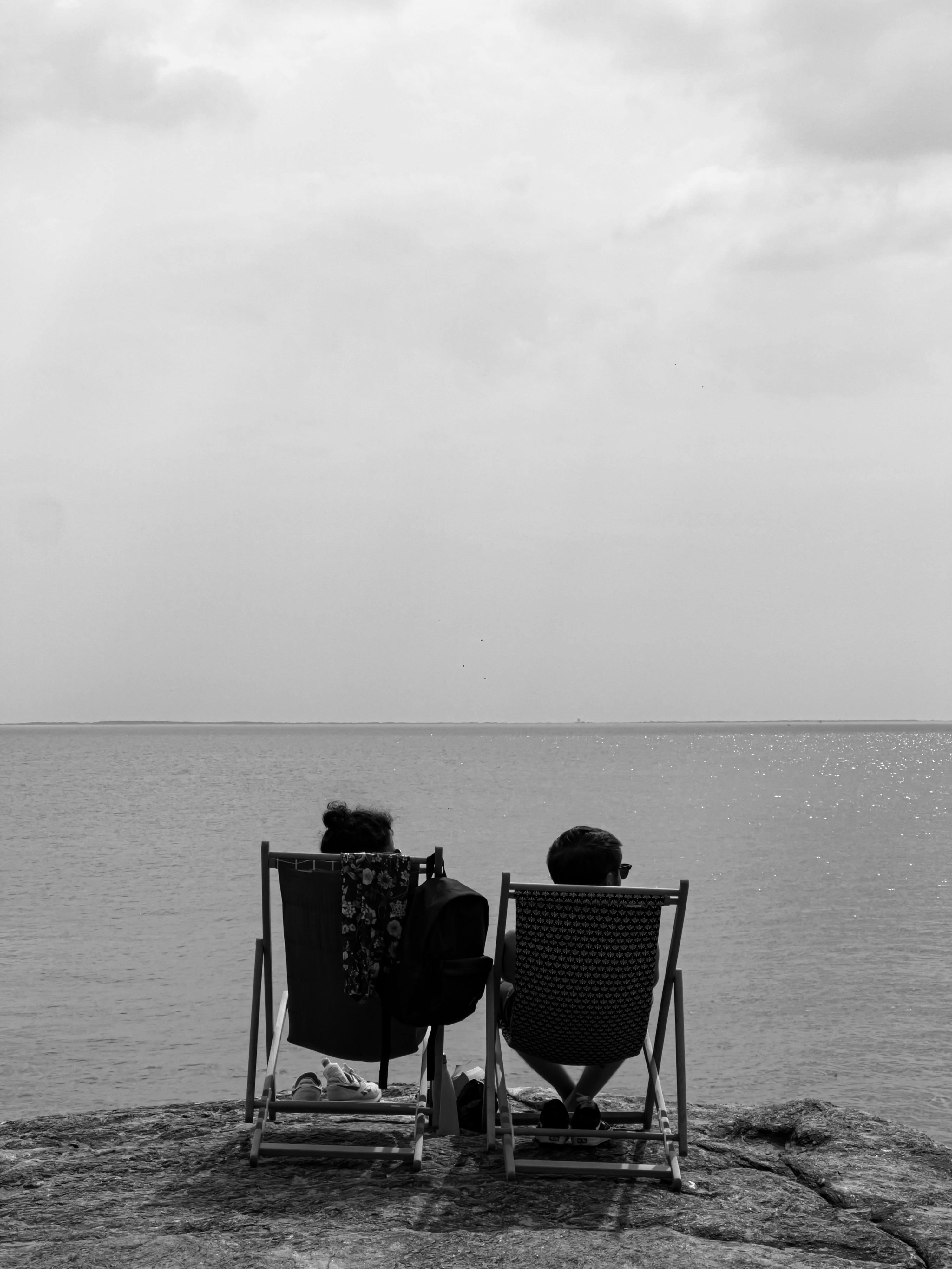 back view of people sitting on folding chairs on a shore