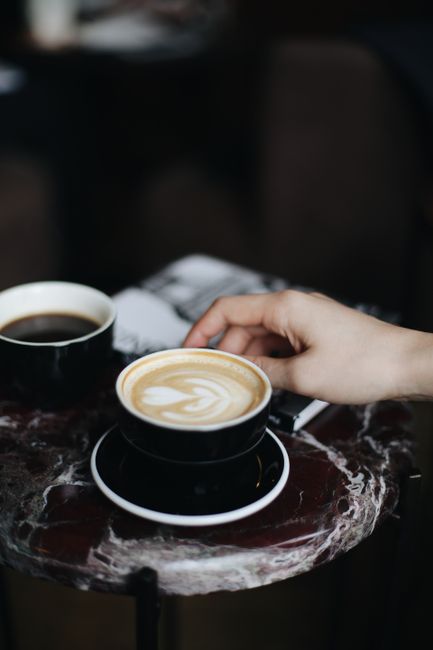 Elegant cappuccino with heart latte art on marble table, accompanied by a hand and coffee cup.
