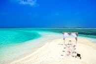 在蔚蓝的天空下，风景如画的海滩婚礼设施旁，是清澈碧绿的海水和白色的沙滩