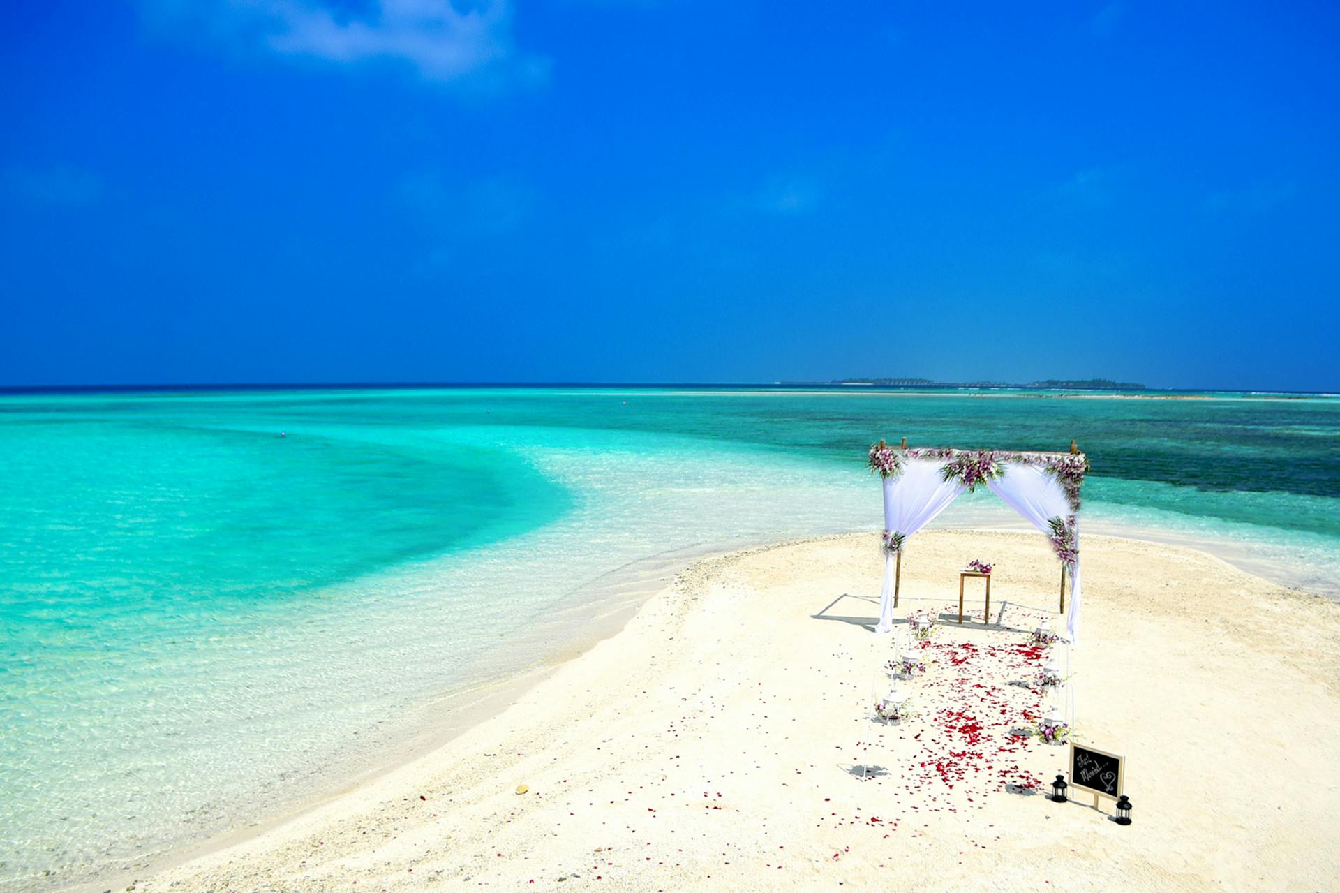 A picturesque beach wedding setup with clear turquoise waters and white sand under a bright blue sky.