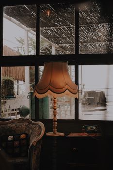 A vintage-style room featuring a classic armchair, elegant lamp, and rainy window view for a cozy atmosphere.