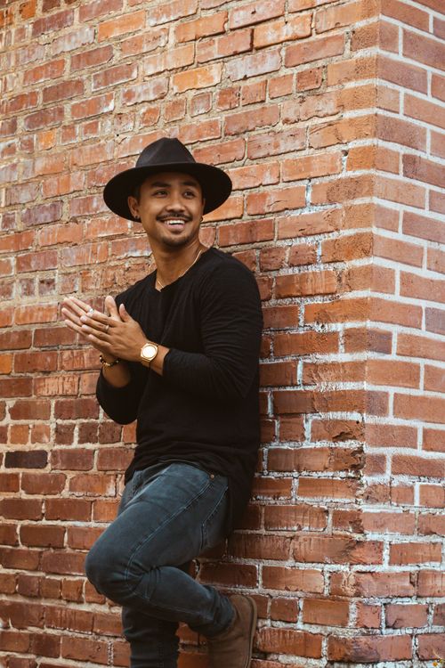 Free Fashionable man in casual wear smiling and clapping in front of a brick wall outdoors. Stock Photo
