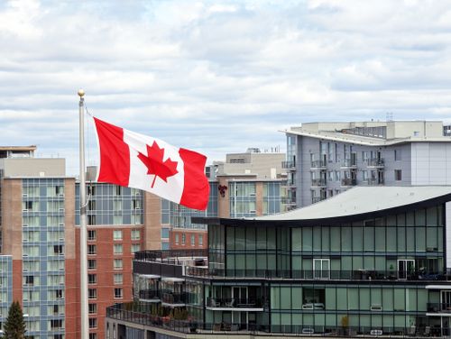 Free Canadian flag waving prominently in Halifax skyline with modern architecture. Stock Photo