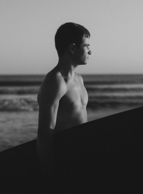 Free Monochrome image of a young male surfer standing by the shoreline with surfboard. Stock Photo
