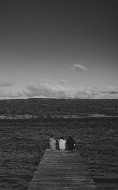 Three friends sit quietly on a wooden pier, enjoying the peaceful lakeside view.