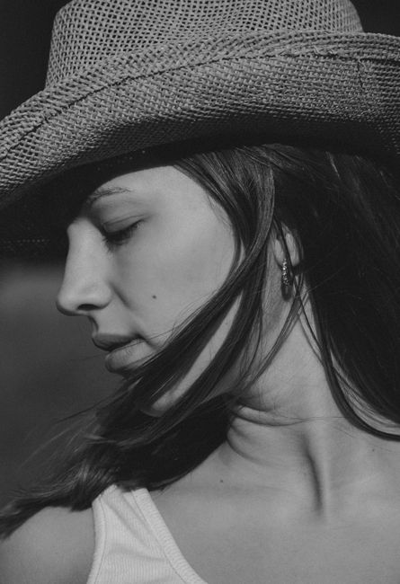 Artistic black and white portrait of a woman in a straw hat with eyes closed.