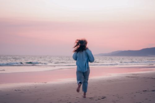 Free Woman jogging on a serene beach at sunset, capturing a moment of freedom and tranquility. Stock Photo