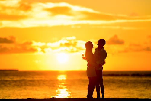 Silhouettes of romantic couple enjoying majestic sunset on seaside