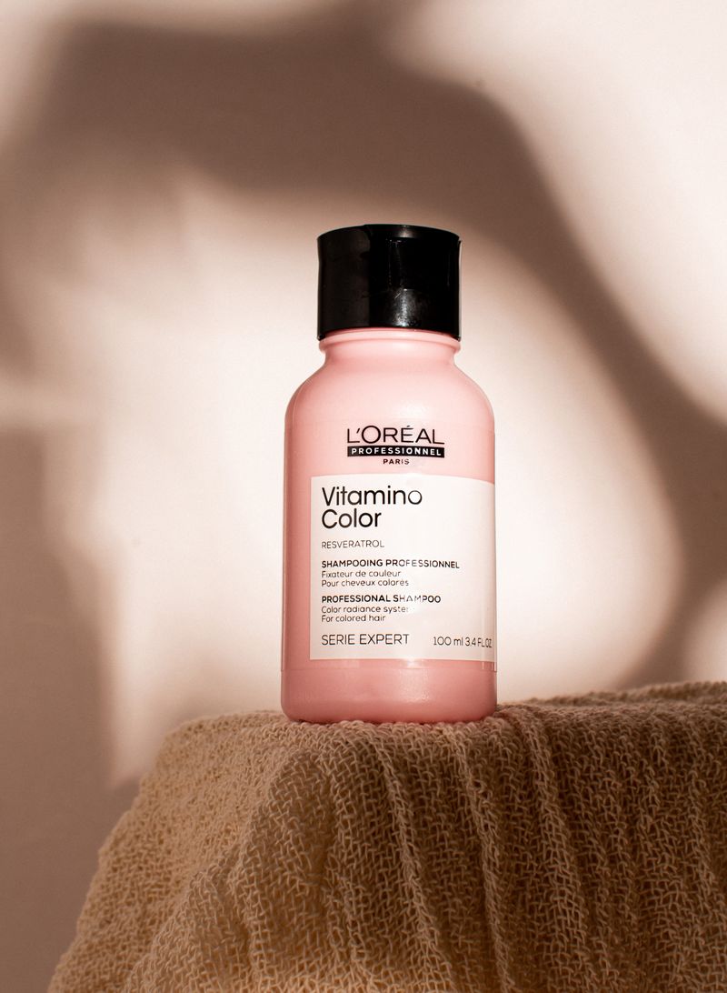 A single shampoo bottle casting soft shadows on textured neutral fabric