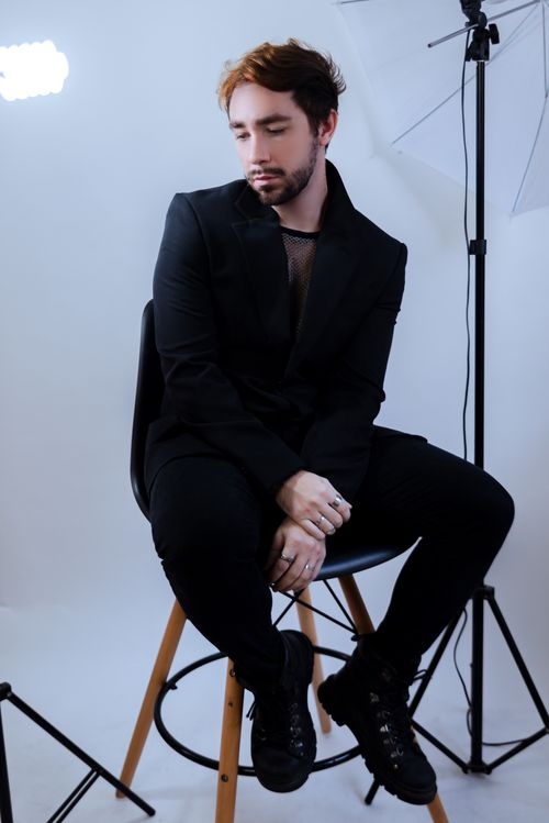 Free A male model in a black suit sitting on a chair in a photography studio with lighting equipment. Stock Photo