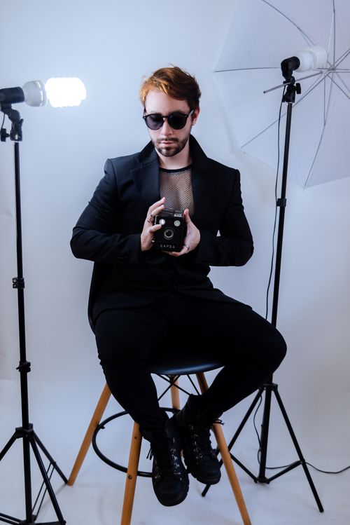 Free Fashion photographer in black suit holding vintage camera during a photo shoot on white background. Stock Photo