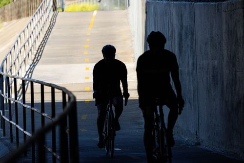 Free Shadowy silhouettes of cyclists riding through a sunlit urban tunnel, creating a striking contrast. Stock Photo