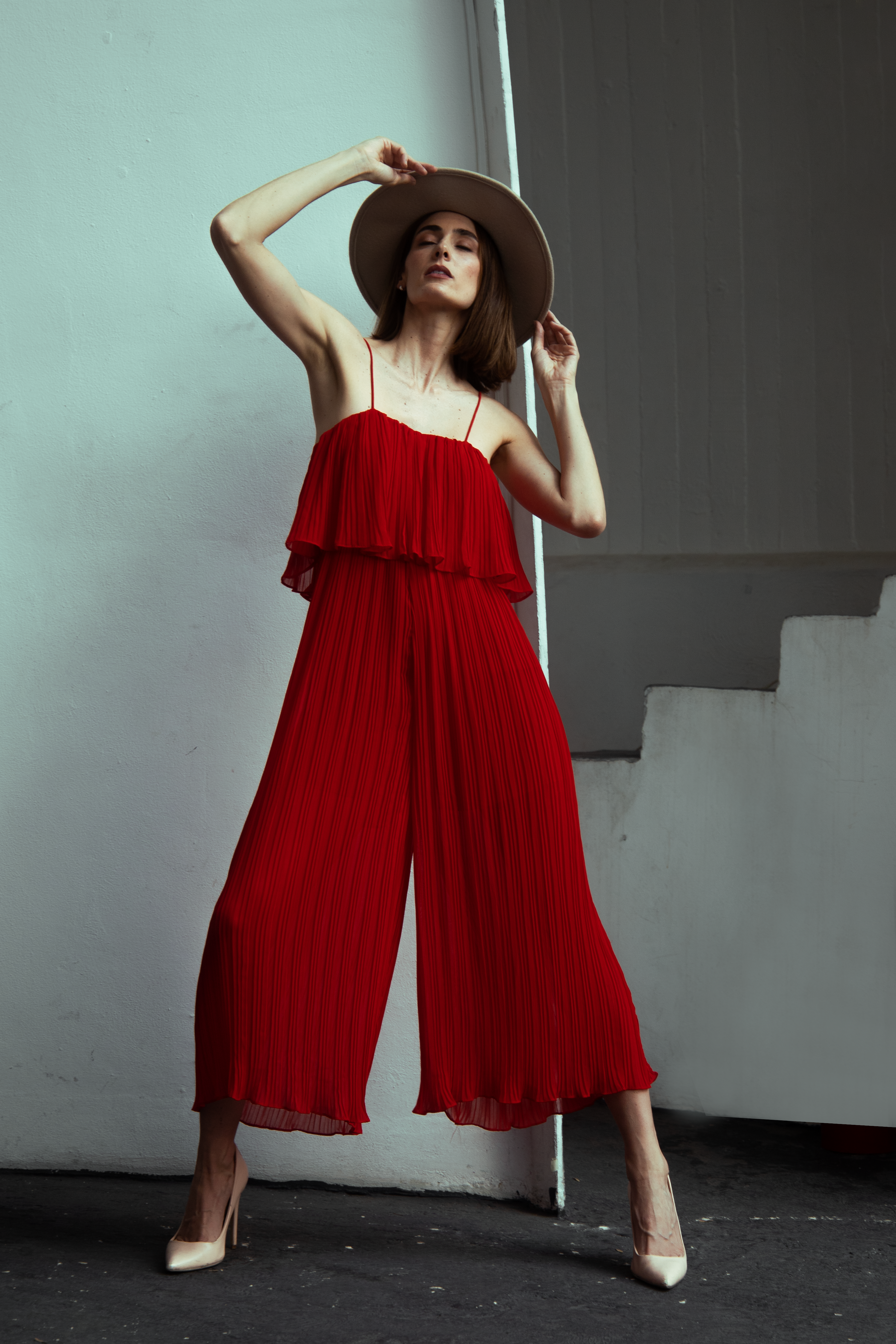 Fashionable woman in a red dress and hat standing against a wall in Mexico City.