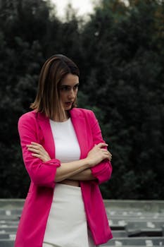 Stylish woman in a pink jacket poses outdoors, embodying elegance and modern fashion.