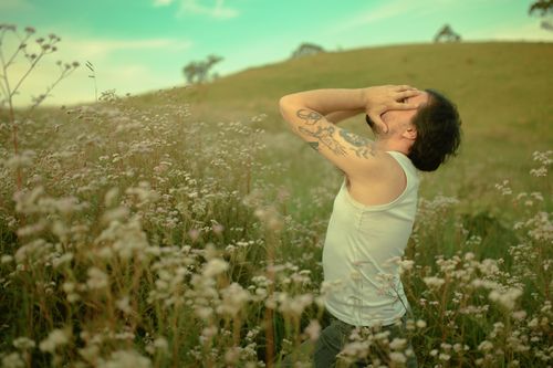Free A man in a meadow with tattoos expresses emotion, standing among wildflowers. Stock Photo
