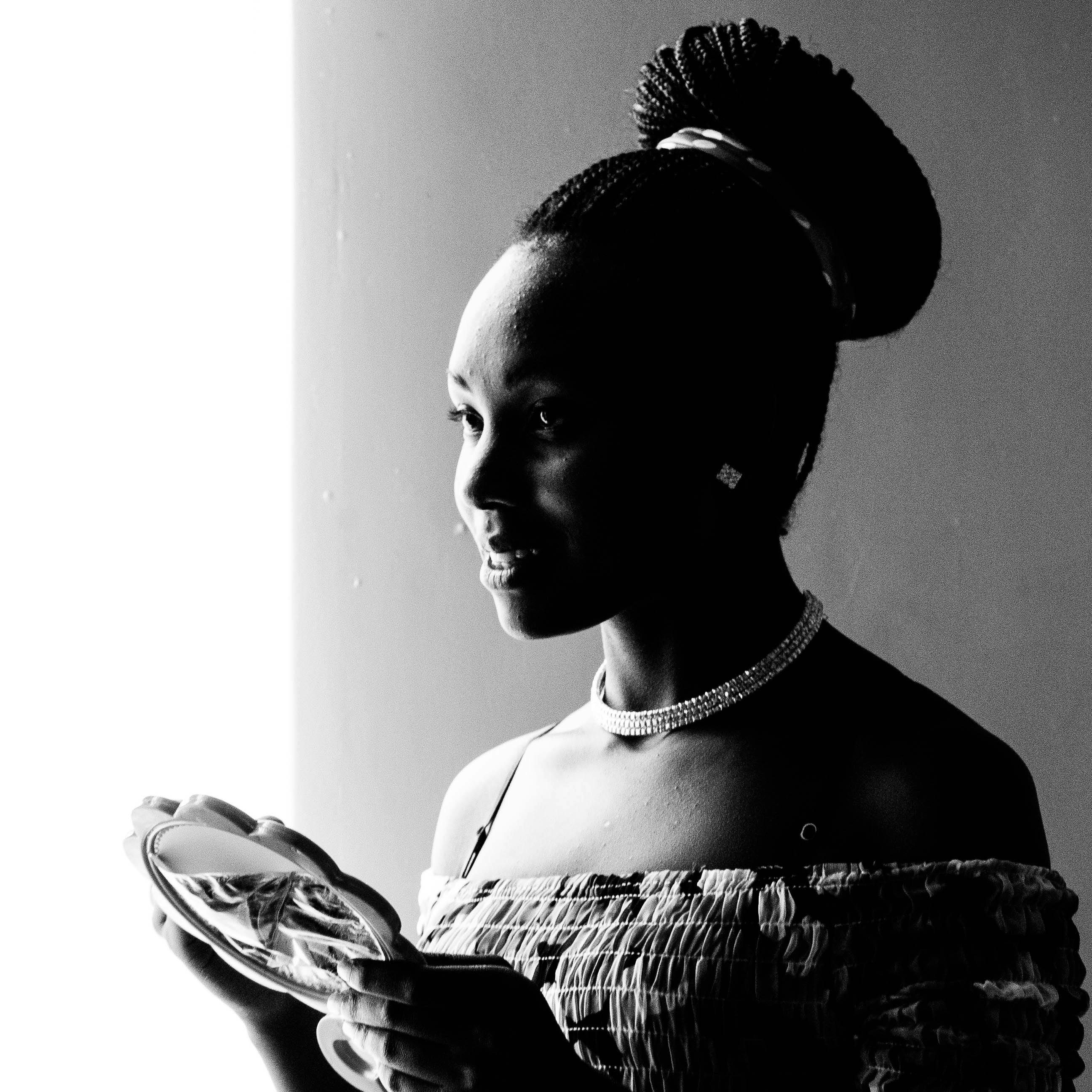 一幅黑白肖像中，一位微笑的女人编着辫子，手拿一面镜子