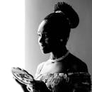 一幅黑白肖像中，一位微笑的女人编着辫子，手拿一面镜子