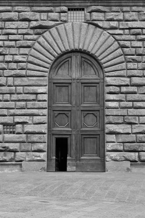 Black and White Photo of Large Wooden Door in a Stone Wall 