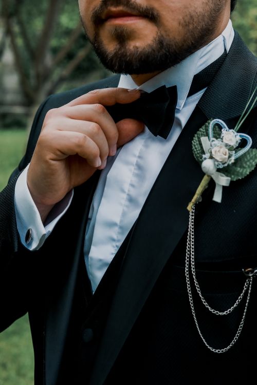 Free Close-up of a groom in a black suit and bow tie adjusting his attire outdoors, ready for his wedding. Stock Photo