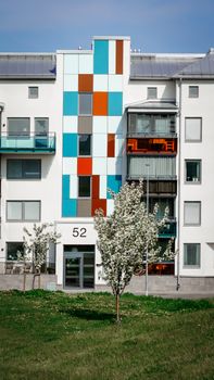 Contemporary apartment building with colorful facade and spring trees in front, creating a lively residential scene.