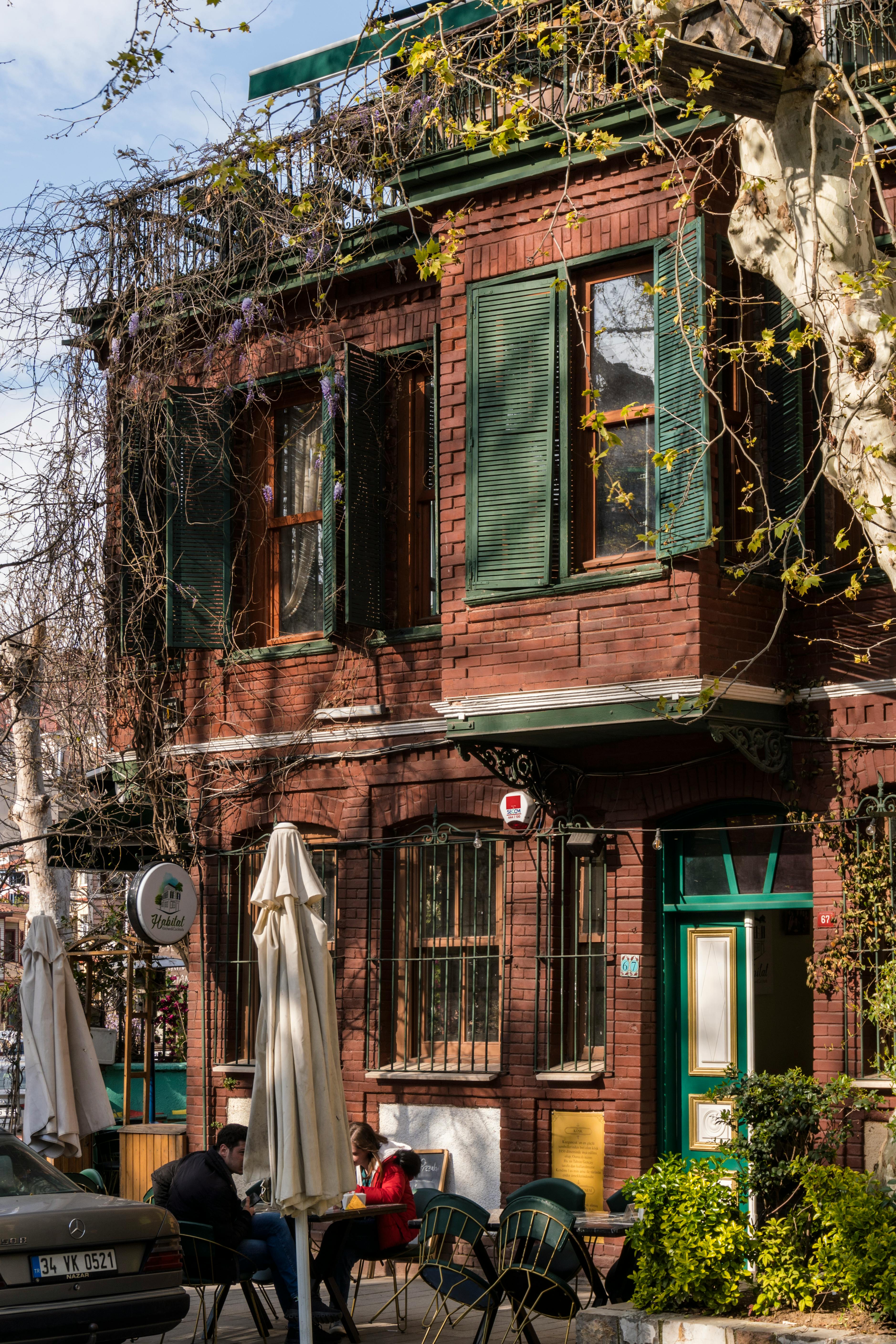 Free A cozy urban street scene featuring a brick house with green shutters and outdoor seating. Stock Photo