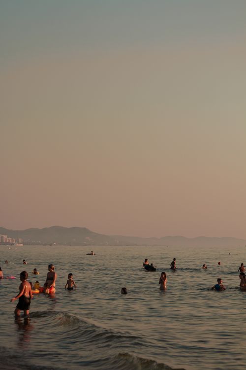Free People enjoying a tranquil evening swim at Durrës beach, Albania, with the sunset casting a warm glow. Stock Photo