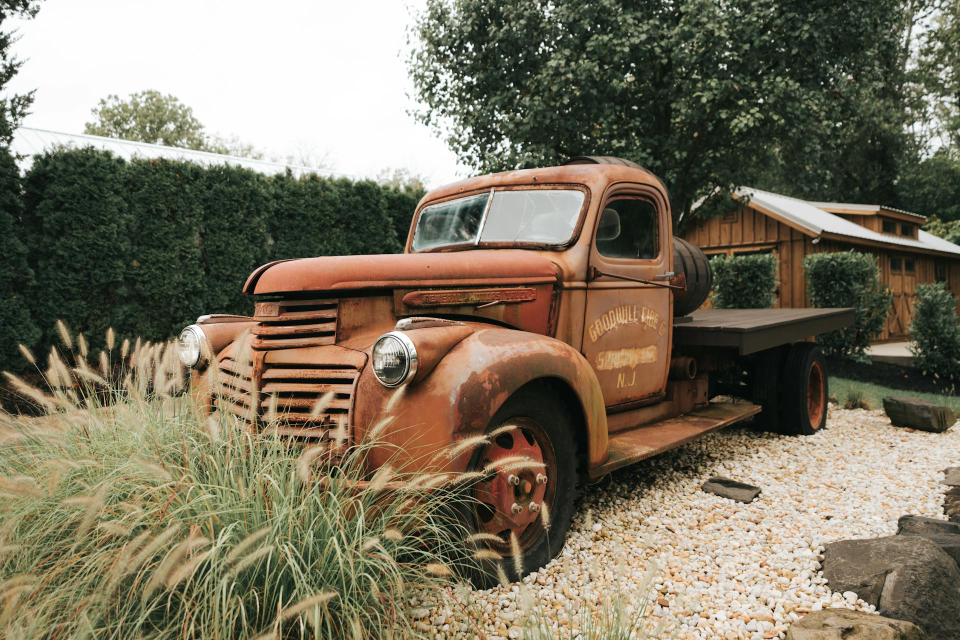 A classic rusty truck parked outdoors, surrounded by greenery and gravel, evoking a vintage charm.