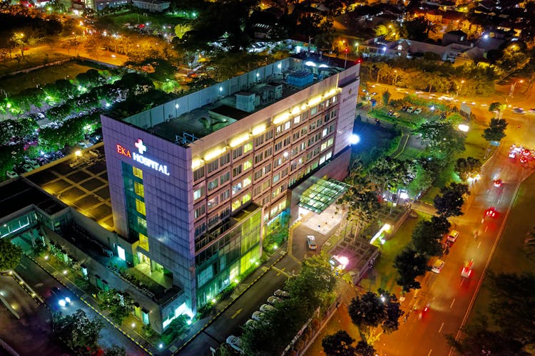 Hospital Beside Vehicle Park And Road At Night