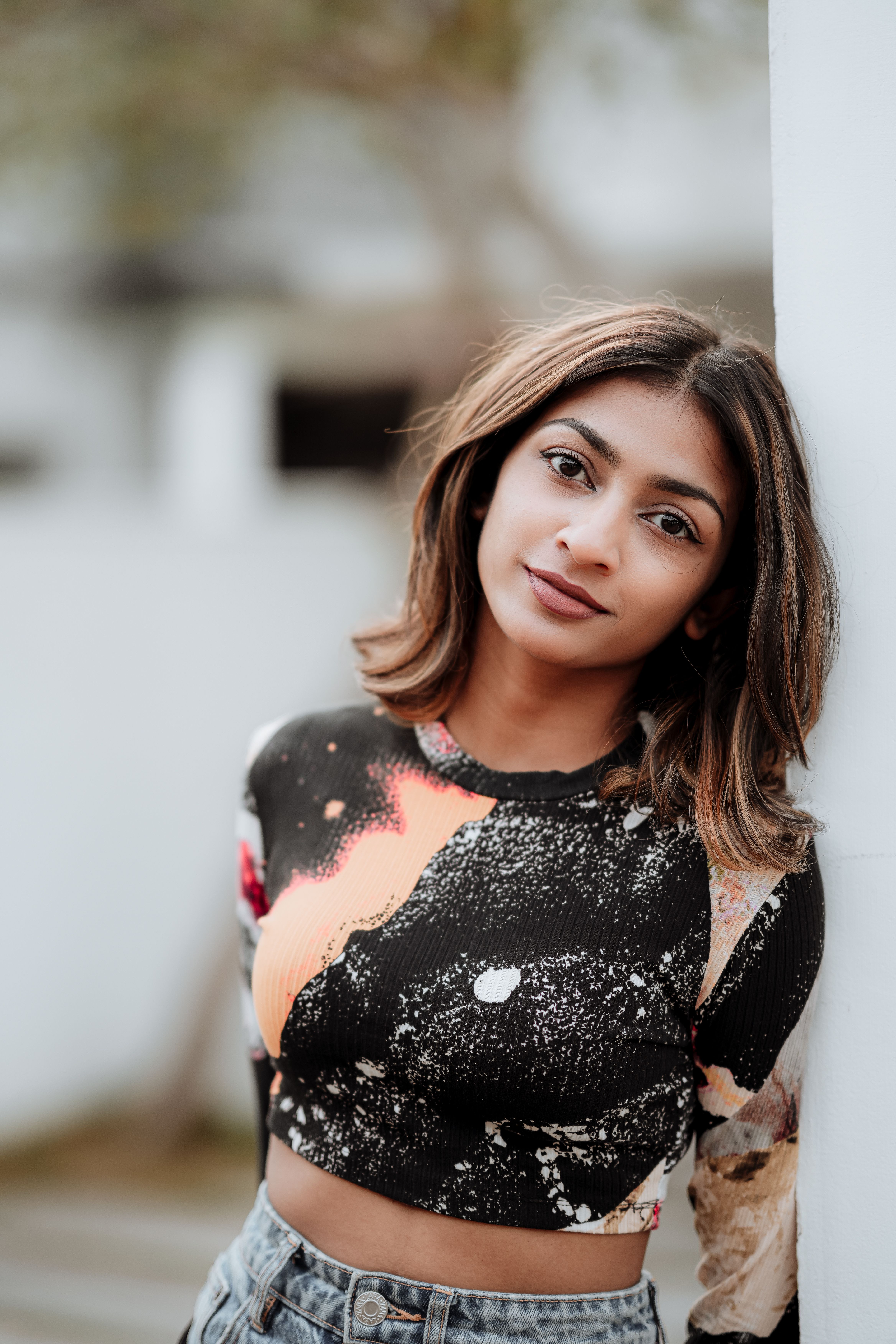 Young woman in trendy outfit leaning on a wall outdoors, showcasing casual urban style.