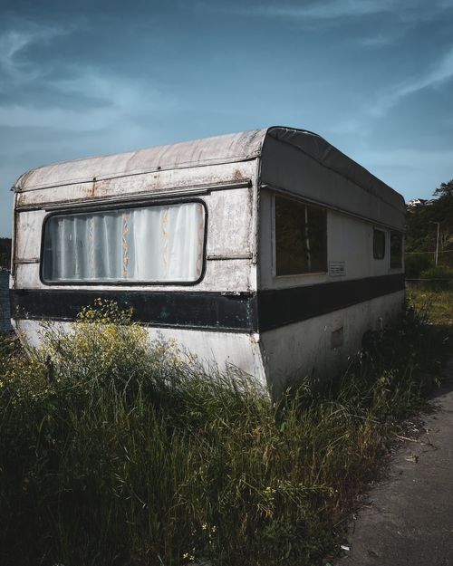 Free Old caravan left in a grassy field, showcasing decay and abandonment under a clear sky. Stock Photo