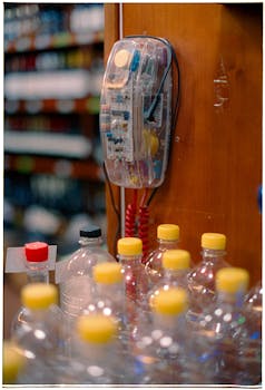 Plastic bottles with yellow caps near a vintage wall phone in a store setting.
