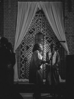 A black and white photo of a woman speaking at a microphone during a ceremony in a Kinshasa church.