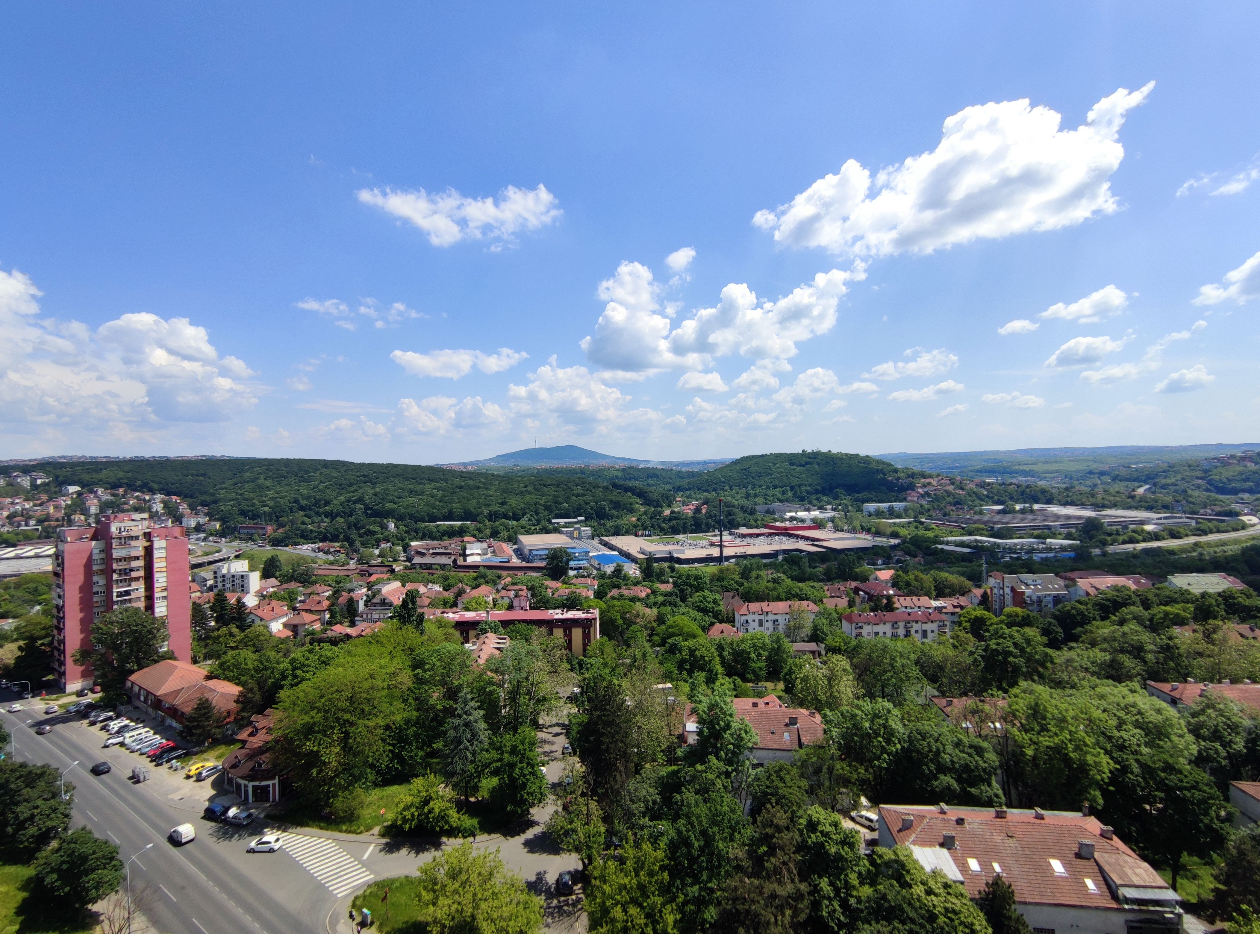 Stunning aerial shot of a green residential district surrounded by hills under a bright blue sky.