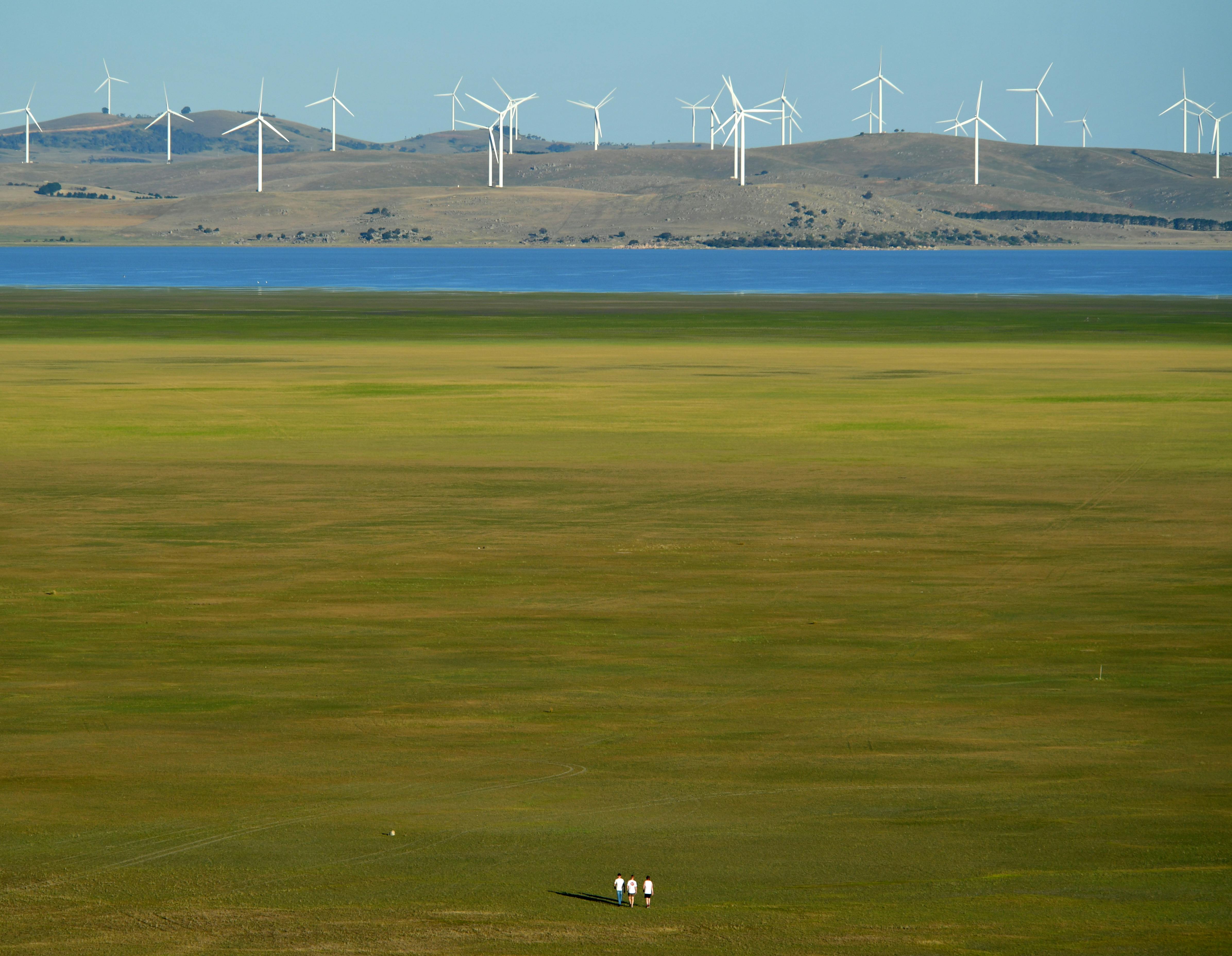 A scenic view of wind turbines near Lake George, Australia, with people walking in the green field.