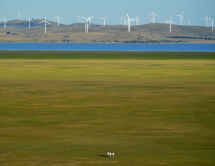 A scenic view of wind turbines near Lake George, Australia, with people walking in the green field.