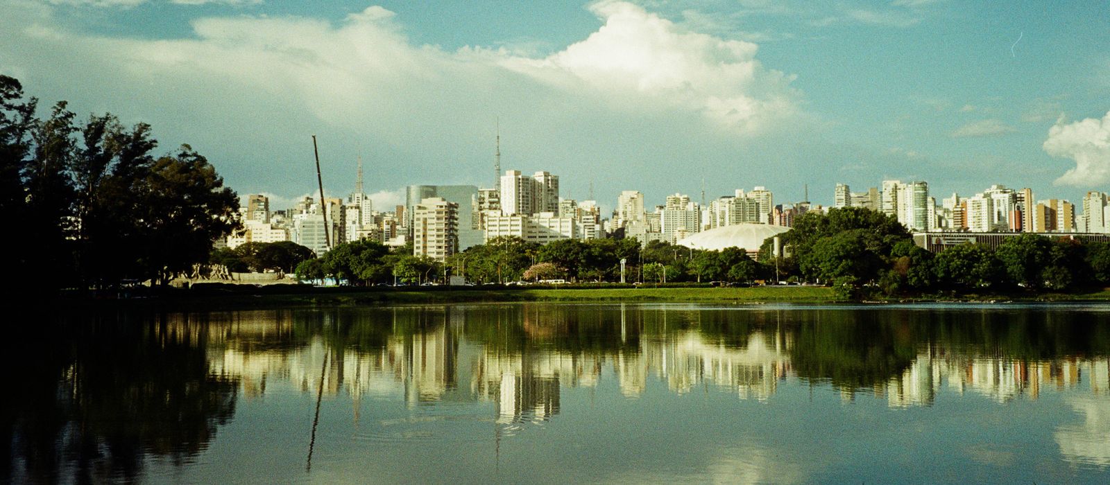 A stunning view of São Paulo's skyline reflected in the calm waters of Ibirapuera Lake, surrounded by lush greenery.