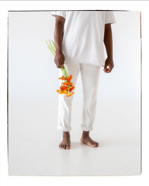 Barefoot person in white clothes holding bright orange flowers