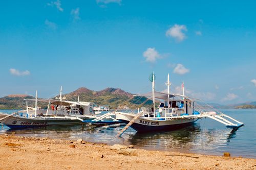 Free Jukung boats rest peacefully by the clear blue sea under a bright sky in the Philippines. Stock Photo