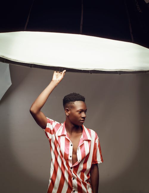 Young Man in Striped Shirt Holding the Edge of a Big Lamp