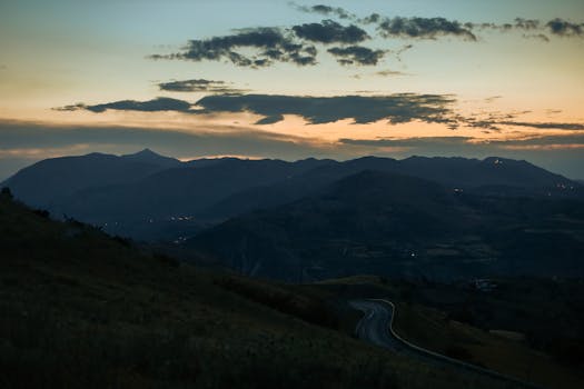 Captivating view of a mountain range at twilight with winding road and serene sky.