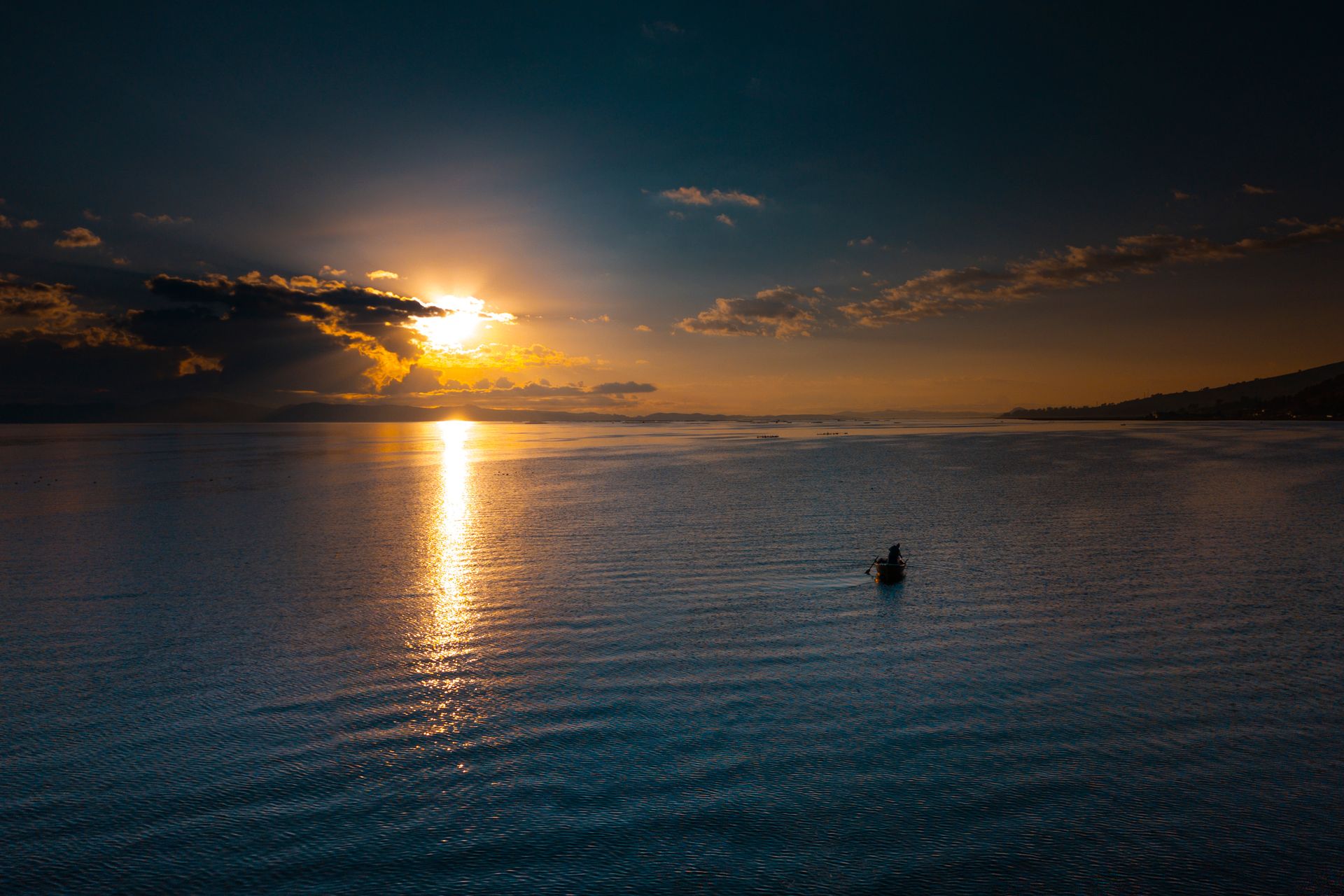 A tranquil view of Lake Titicaca at sunset, featuring a lone boat under dramatic skies in Puno, Peru.