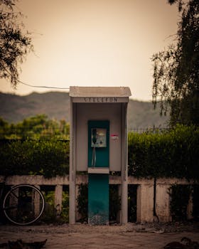 A nostalgic vintage phone booth surrounded by urban greenery at sunset.