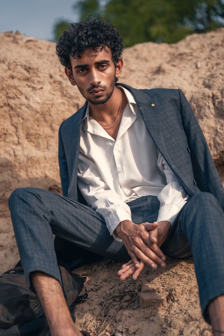 Model In A Checked Gray Suit And A White Shirt Sitting On A Pile Of Dirt