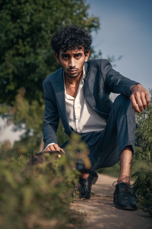 Free Man in a gray suit crouching on a pathway outdoors in Faisalabad, Pakistan Stock Photo