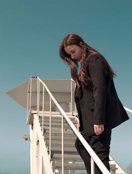 Elegant woman in a suit on airstairs against a clear sky, conveying modern fashion vibes.